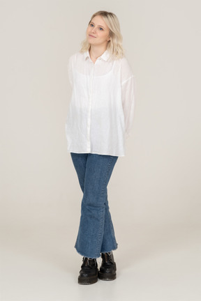 Front view of a shy blonde female in casual clothes crossing legs and looking aside