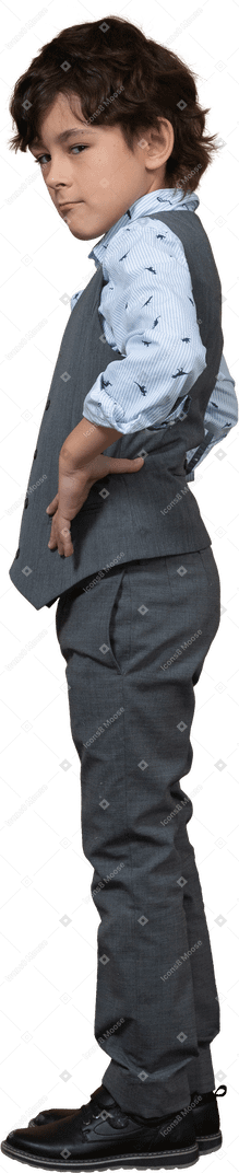 Vista laterale di un ragazzo carino in abito grigio in posa con le mani sui fianchi