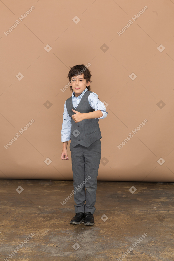 Vista frontal de un chico lindo con traje gris que muestra el pulgar hacia arriba