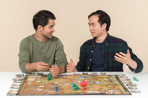 Interracial male friends sitting at the table and playing board game