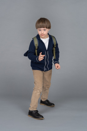 Portrait d'un petit garçon avec un sac à dos levant la main