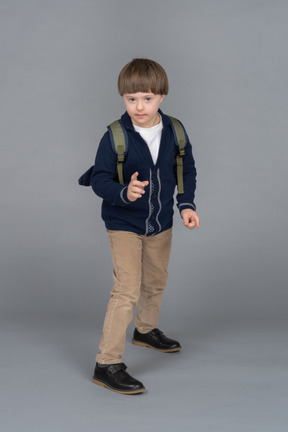 Portrait of a little boy with a backpack holding up a hand