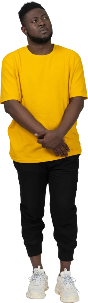 Front view of a shy young dark-skinned man in yellow t-shirt holding hands together