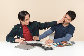 Deux jeunes geeks assis à la table en train de réparer quelque chose et l'un d'eux distrait l'autre