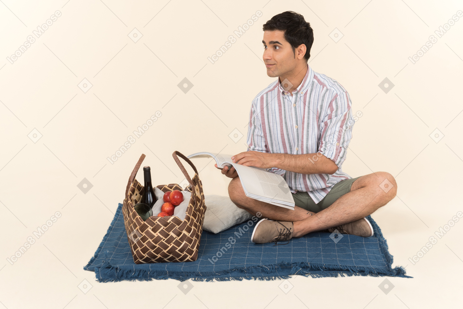 年轻的白种人坐在毯子上，拿着杂志打开