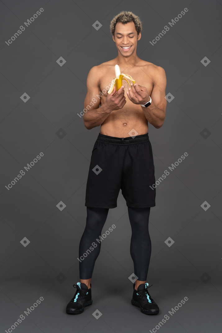 Vista frontal de un sonriente hombre afro sin camisa pelando el plátano