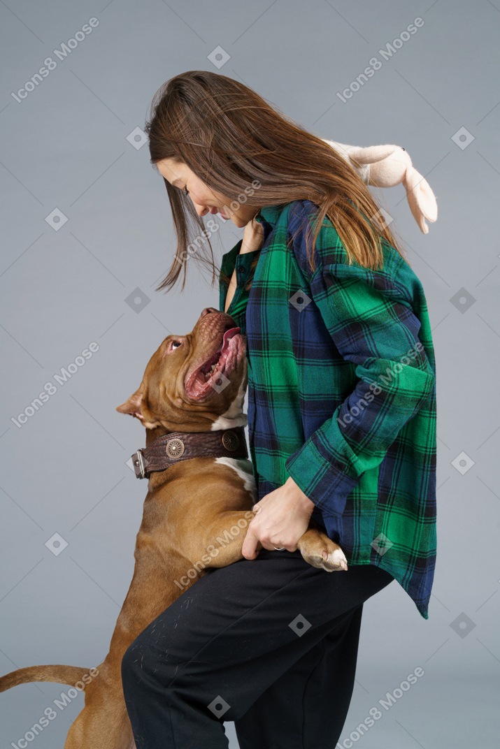 Sid view of a brown bulldog hugging young female in checked shirt
