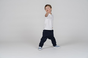 Three-quarter view of a boy pointing at the camera and looking aside