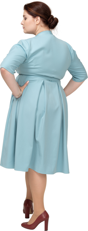 腰に手でポーズをとって青いドレスを着た女性の背面図