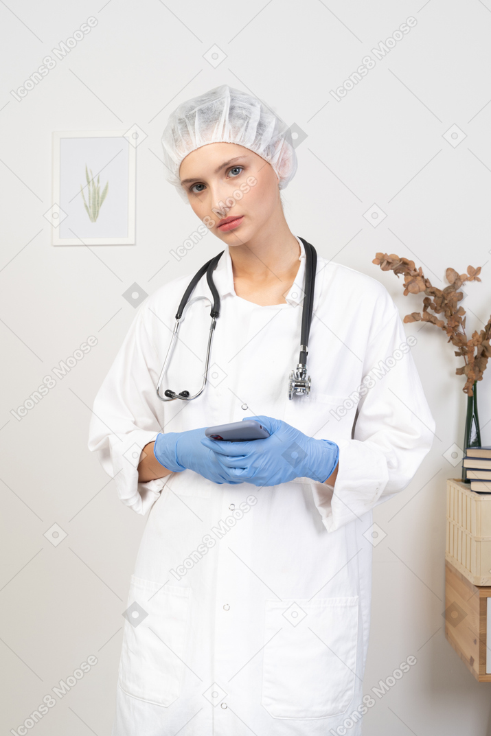 Front view of a young female doctor with stethoscope holding her phone