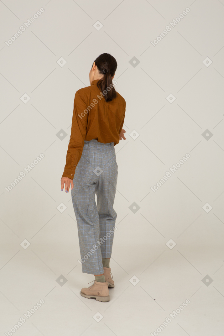 Vista traseira de uma jovem mulher asiática de calça e blusa fazendo uma reverência