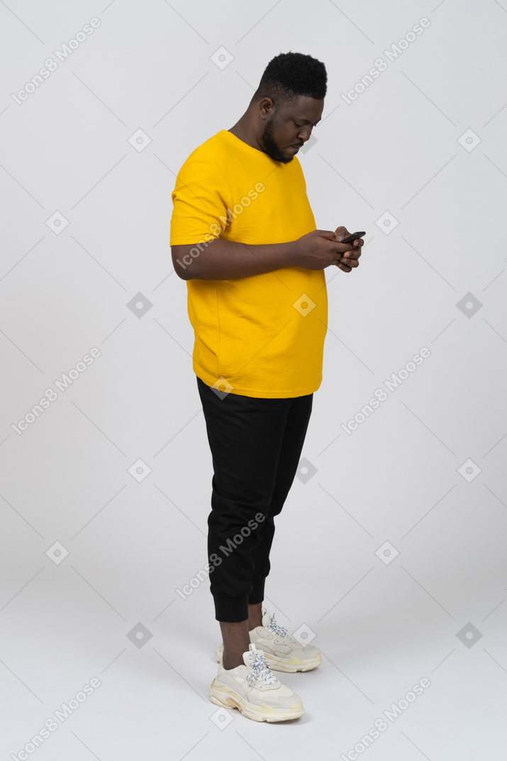 전화로 채팅하는 노란색 티셔츠를 입은 검은 피부의 젊은 남자의 3/4 보기