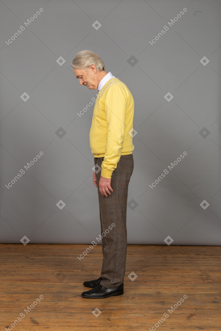一个黄色的套衫弯下腰，他的眼睛的可悲的老男人的侧视图