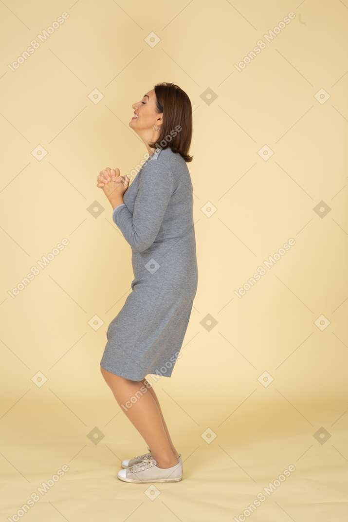 Вид сбоку женщины в сером платье, делающей молитвенный жест