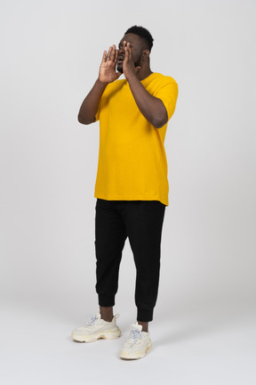 Vista de tres cuartos de un joven de piel oscura gritando en camiseta amarilla