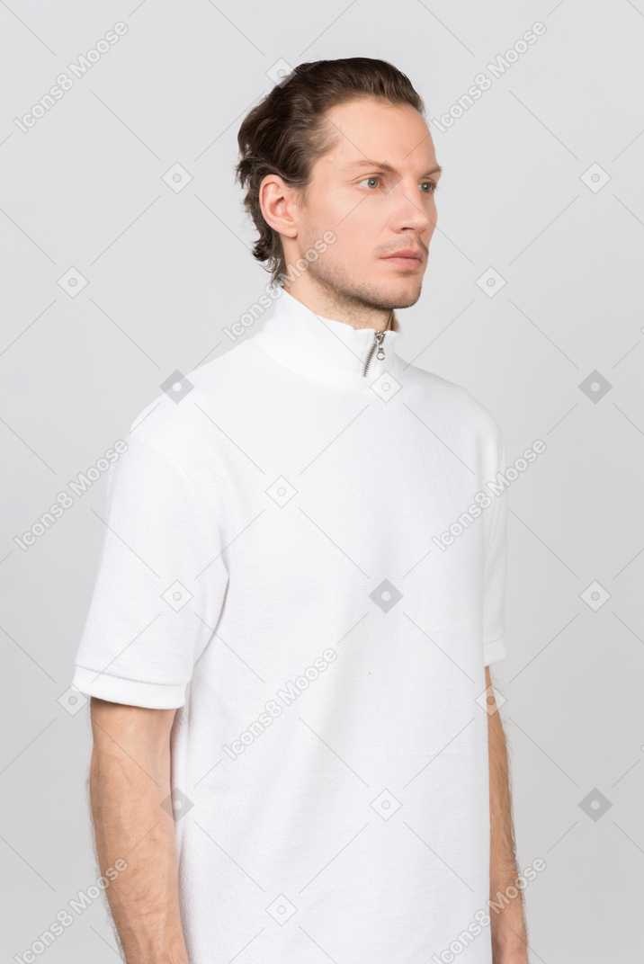 Jeune homme en t-shirt polo blanc debout à moitié face à la caméra
