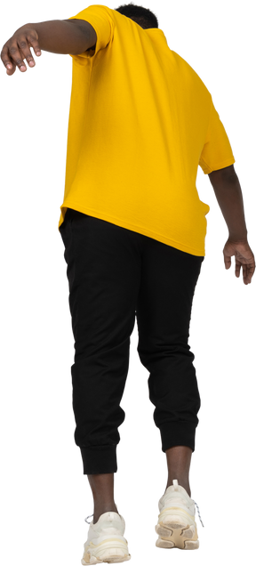 Back view of a young dark-skinned man in yellow t-shirt leaning forward & outstretching arm