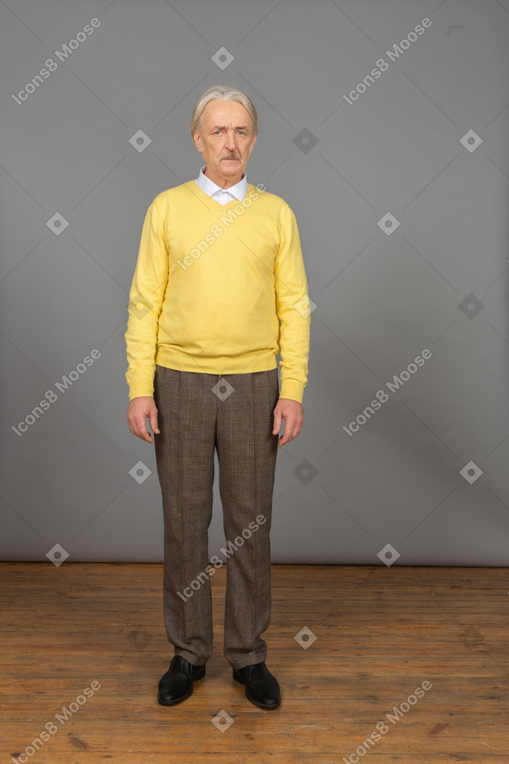 Front view of a displeased old man wearing yellow pullover and looking at camera