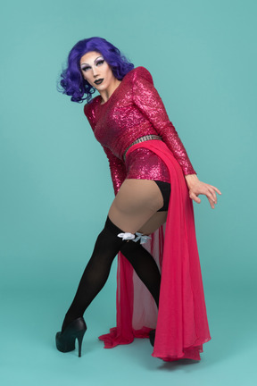 Drag queen com vestido de lantejoulas rosa, inclinando-se para a frente e virando-se