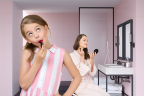 A little girl and woman applying lipstick in bathroom