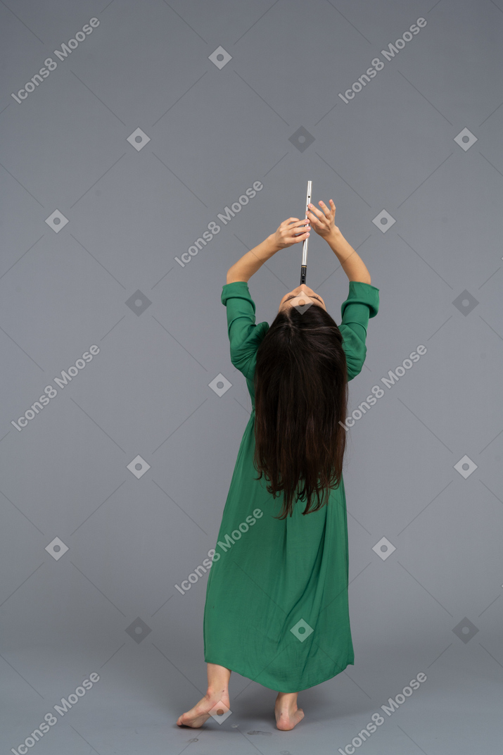 Вид сзади молодой леди в зеленом платье, играющей на флейте, откинувшись назад