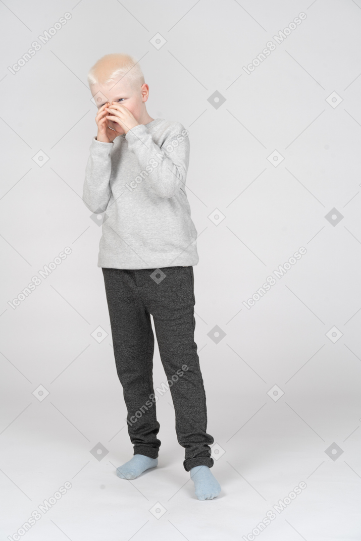 Vista de tres cuartos de un niño que cubre su boca con las manos
