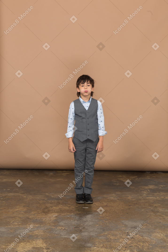 Front view of a cute boy in grey suit puffing cheeks