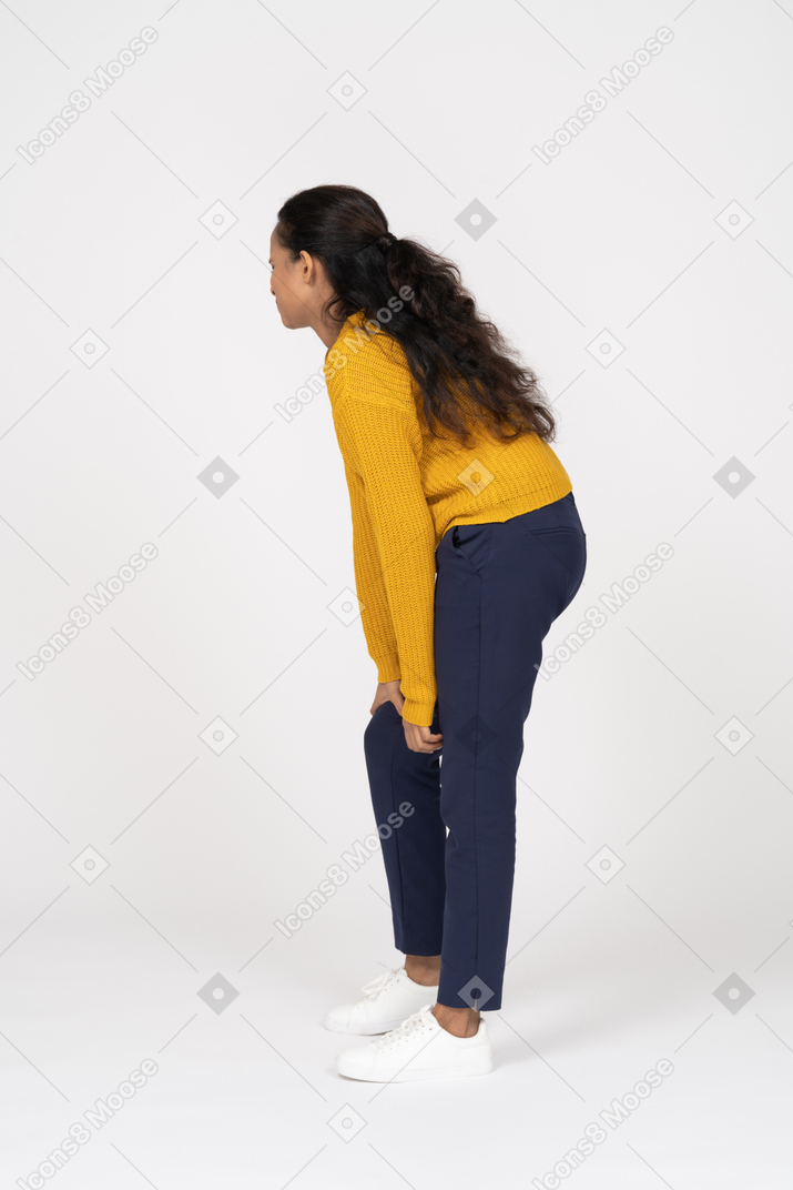Vista lateral de una niña en ropa casual agachándose y tocando su rodilla lastimada