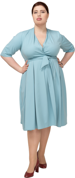 Front view of a woman in blue dress standing with hands on hips and making faces