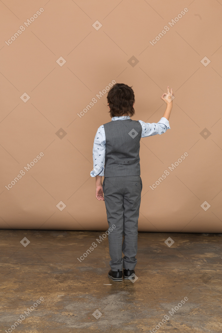 Vista posteriore di un ragazzo in abito grigio che mostra segno ok