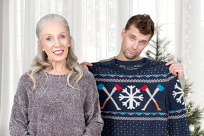 A man trying on a christmas sweater and standing next to an old woman