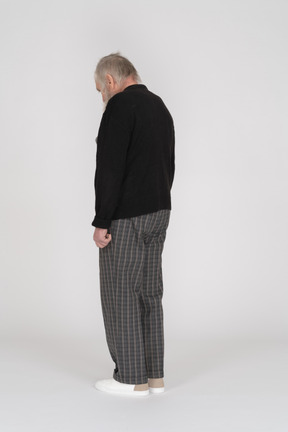 Three quarter back view of an old man standing with head down