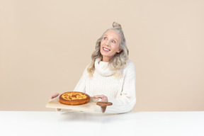 Elegante alte frau mit einem frisch gebackenen kuchen zufrieden