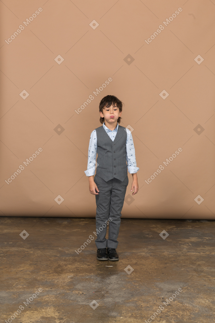 Front view of a cute boy in grey suit puffing cheeks