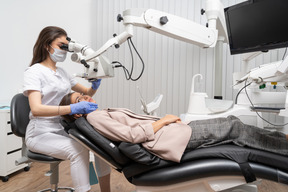 Pleine longueur d'une femme dentiste examinant sa patiente et regardant à travers le microscope