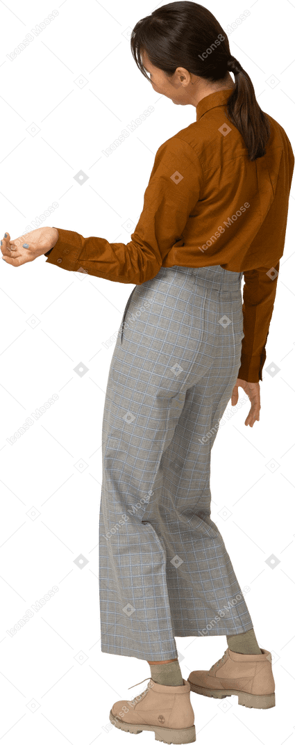 Vista posteriore di tre quarti di una giovane donna asiatica in calzoni e camicetta inclinando la testa e allungando la mano