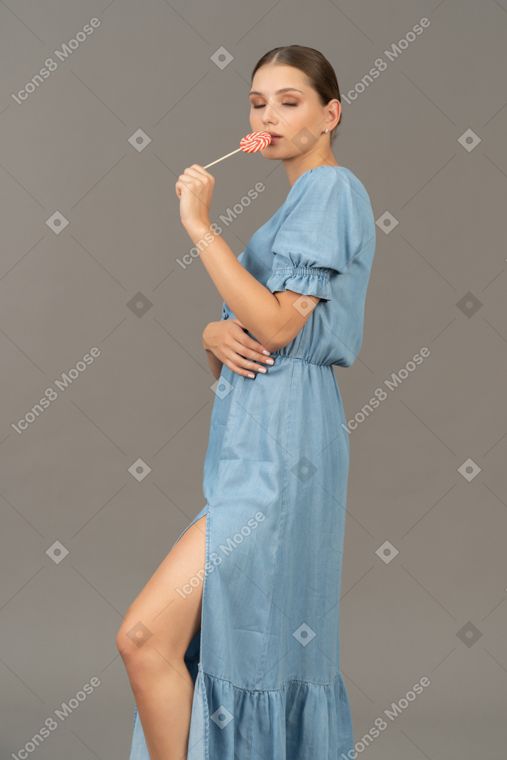 Three-quarter view of a young woman in blue dress holding a lollipop