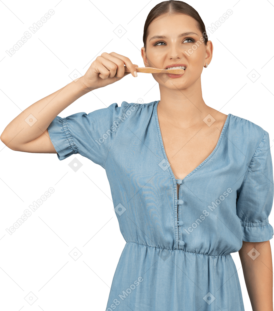 Front view of a young woman in blue dress brushing her teeth