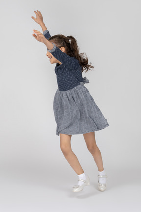 Three-quarter view of a girl running happily with hands up in the air
