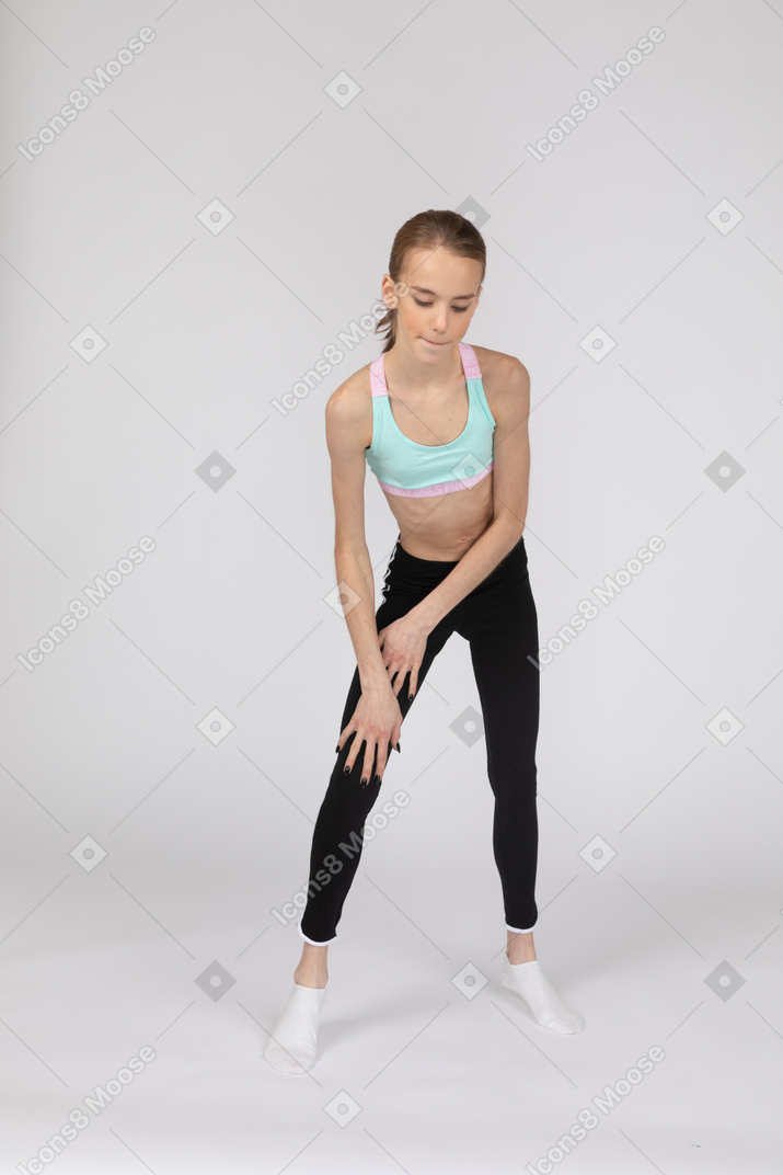 Front view of a teen girl in sportswear touching leg and leaning forward