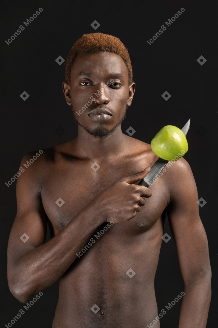 Primo piano un giovane serio che tiene il coltello con una mela su di esso