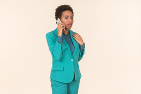 Jovem negra com um corte de cabelo curto, posando em uma roupa azul com um telefone celular na mão