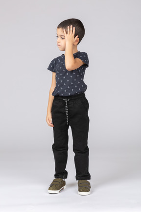 Vista frontale di un ragazzo in abiti casual in piedi con una mano sulla testa
