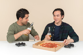 Interracial friends eating pizza, drinking beer and playing video game