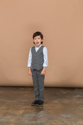Vista frontal de un chico lindo en traje gris haciendo muecas y mostrando la lengua