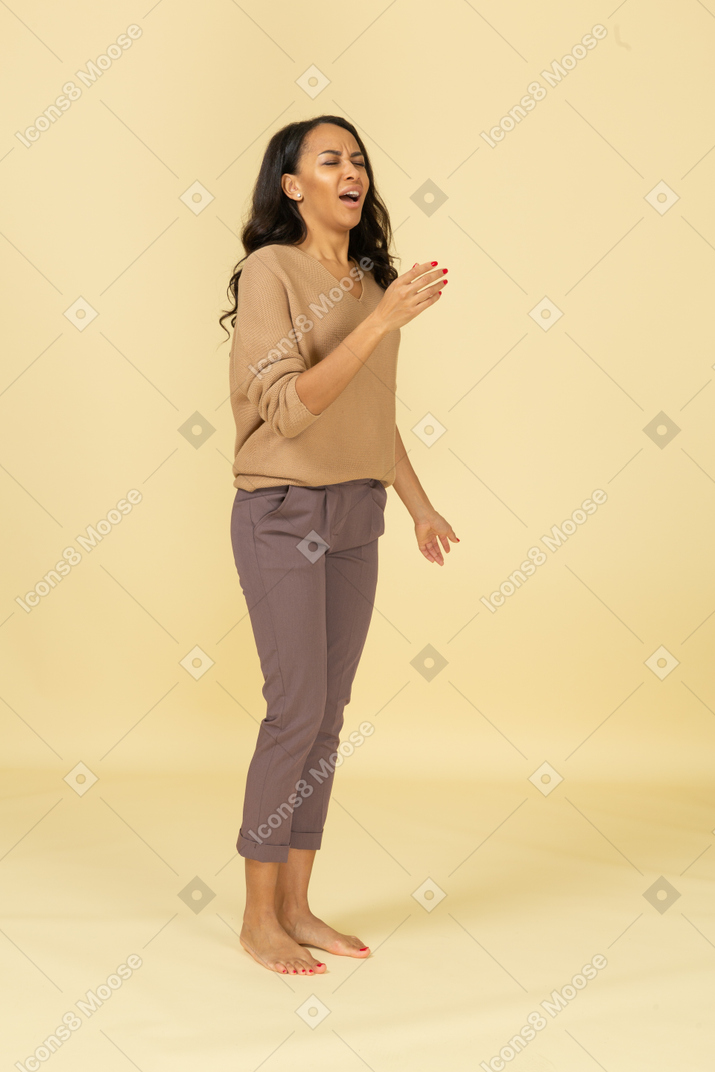Vista de três quartos de uma jovem mulher de pele escura falando levantando a mão