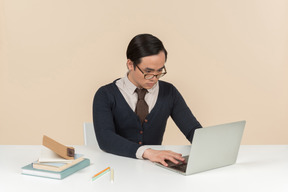Молодой азиатский студент в свитере печатает на ноутбуке