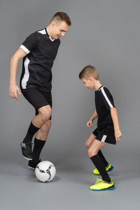 De cuerpo entero de un joven entrenando a un niño pequeño cómo jugar fooyball