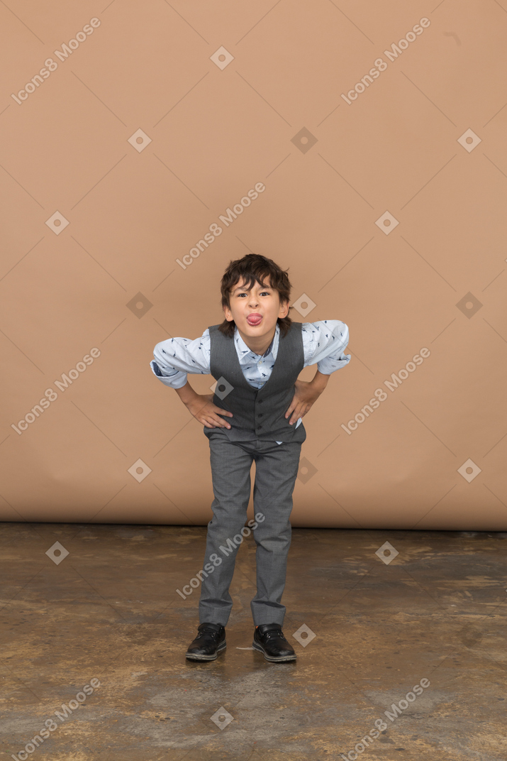 Front view of a boy in suit standing with hands on hips and bending down