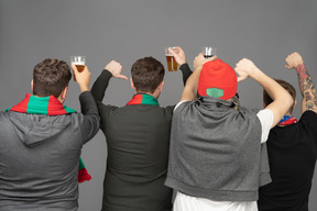 Back view of four displeased male football fans showing thumbs down & holding beer